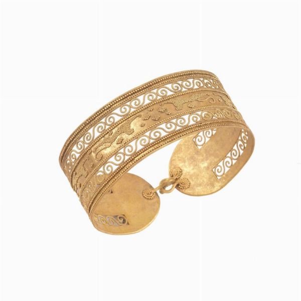 BRACCIALE RIGIDO STILE ARCHEOLOGICO MICROGRANULATOin oro giallo 18kt, raffigurante un fregio decorativo traforato e lavorato con la tecnica della granulazione, dim. cm 6,5x6 circa, gr. 34  ARCHAELOGICAL STYLE MICRO-GRANULATED BANGLE IN 18KT YELLOW GOLD  - Asta Gioielli in stile archeologico  - Associazione Nazionale - Case d'Asta italiane