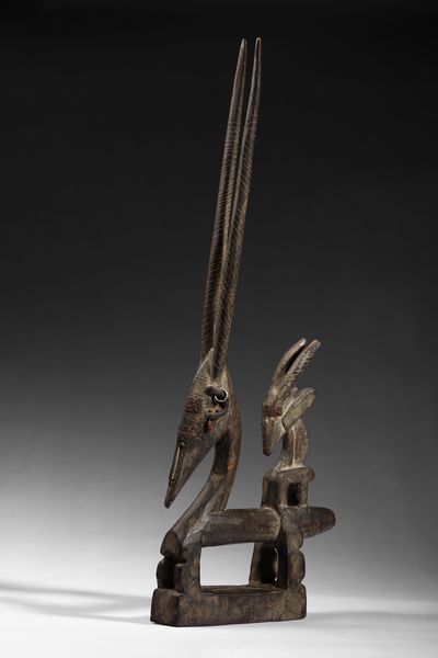 Bambara - Mali : Cimiero da danza  o Chiwara  a forma  di scultura zoomorfa  raffigurante un'antilope stilizzata con il suo piccolo in piedi sulla schiena.Legno duro a patina scura, metallo e tessuto.  - Asta Asta 422 | AFRICA, OCEANIA E AMERICHE - ARTIGIANATO AFRICANO: VARI COMMITTENTI E SELEZIONE DALLA COLLEZIONE BARTOLOMUCCI Online - Associazione Nazionale - Case d'Asta italiane