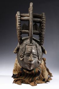 Igbo - Nigeria - Maschera antropomorfa con elaborata acconciatura. Legno a patina scura, pigmenti e tessuti.