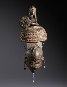 Igbo - Nigeria - Nello stile di Maschera con copricapo sormontato da una scultura di scimmia  in legno a patina scura, fibre,  conchiglie, perline, semi e pelle