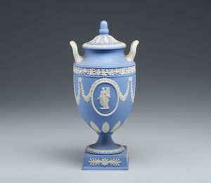 MANIFATTURA DI WEDGWOOD, XX SECOLO - Urna 'all'antica' in ceramica azzurra e bianca con ghirlande floreali e fitomorfe, corpo centrato da figure di Apollo e di una Musa