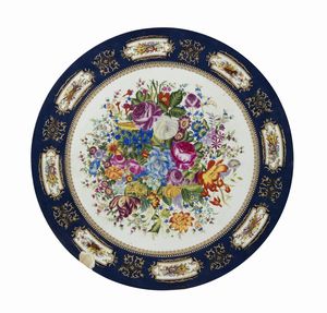 MANIFATTURA DEL XX SECOLO - Grande piano circolare in ceramica dipinto e decorato nello stile di Limoges con trionfo di fiori al centro, fascia esterna a fondo blu con riquadri raffiguranti nature morte di strumenti musicali