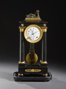 MANIFATTURA FRANCESE DEL XIX SECOLO - Orologio a pendolo in legno ebanizzato e bronzi dorati, quattro colonne a sorreggere il quadrante e la parte superiore, sormontata da figura di Arianna addormentata