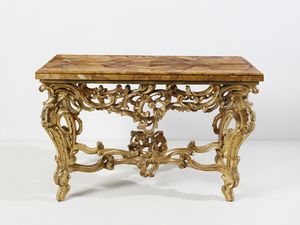 MANIFATTURA ROMANA DEL XVIII SECOLO - Console in legno intagliato e dorato, sostegni in forma di volute e racemi fitomorfi, gambe arcuate unite da traversa a crociera, piano sagomato lastronato in marmo giallo di Siena